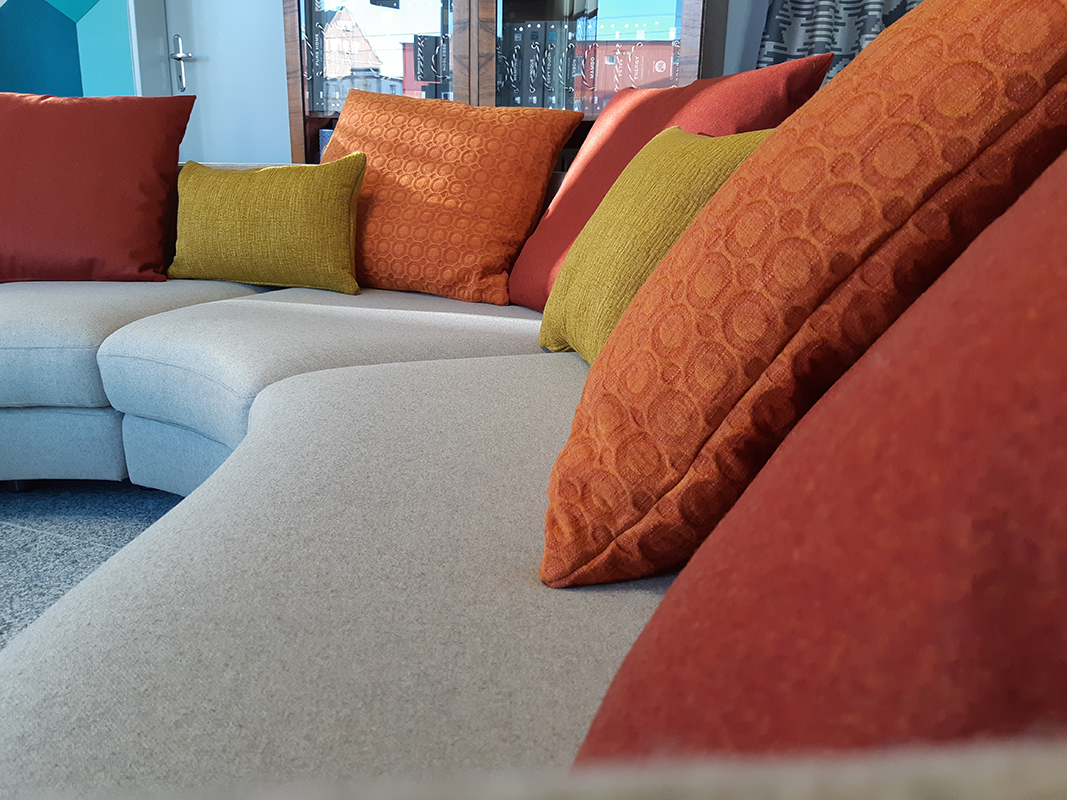 Curved light gray sofa with alternating orange and green decorative pillows in a modern living room.