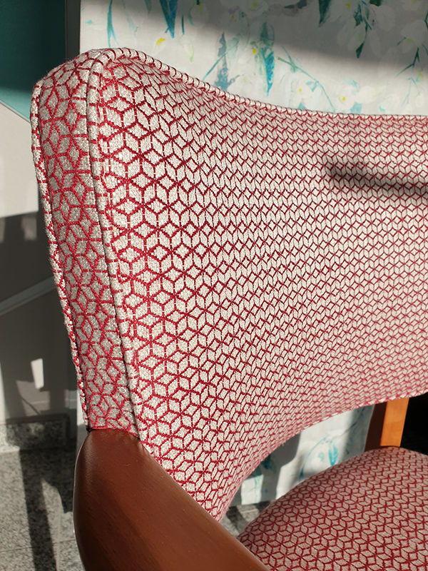Close-up of a chair back and seat with textured red and white hexagonal patterned upholstery and wooden armrests.