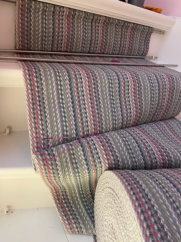 Staircase covered with a striped carpet runner in shades of gray, red, and green with metal stair rods.