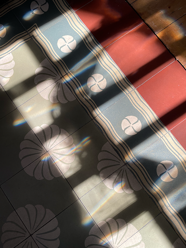 Sunlight casting shadows and light reflections on a patterned tiled floor with circular floral designs and red rectangular tiles along the edge.