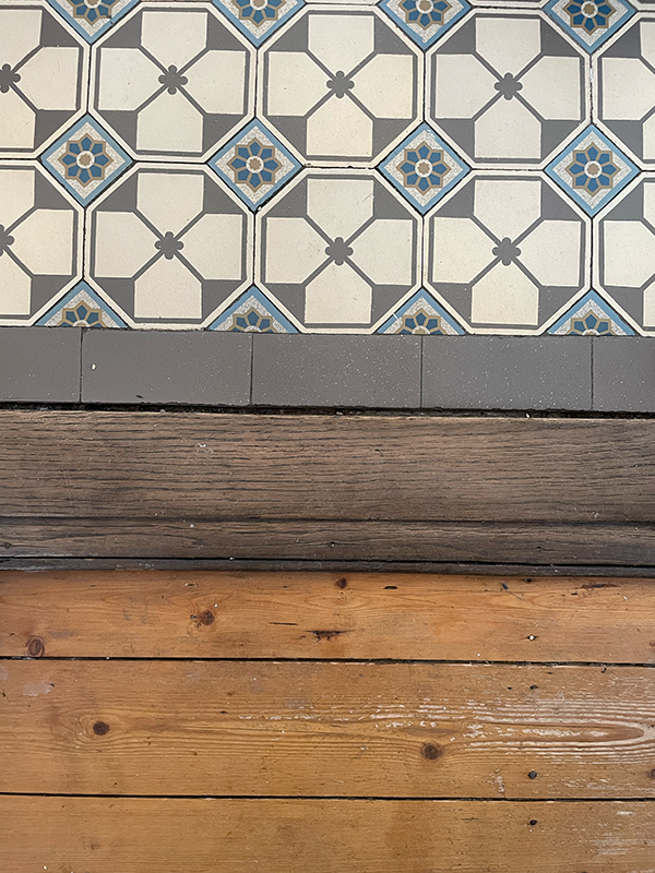 Floor showing a transition from patterned grey, white, and blue tiles to dark and light wooden planks separated by a grey border strip.