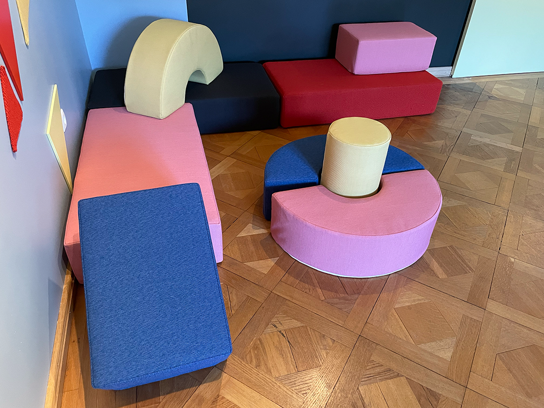 Colorful modular foam seating blocks arranged on wooden parquet floor in a room with blue walls.