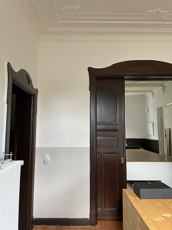 Interior room with white walls, dark wood door frames, a partially open sliding wooden door, and a wooden table with a black box on it.