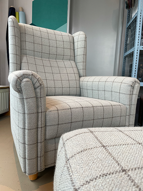 Light gray upholstered armchair with a checkered pattern and rounded armrests, positioned near a matching ottoman.