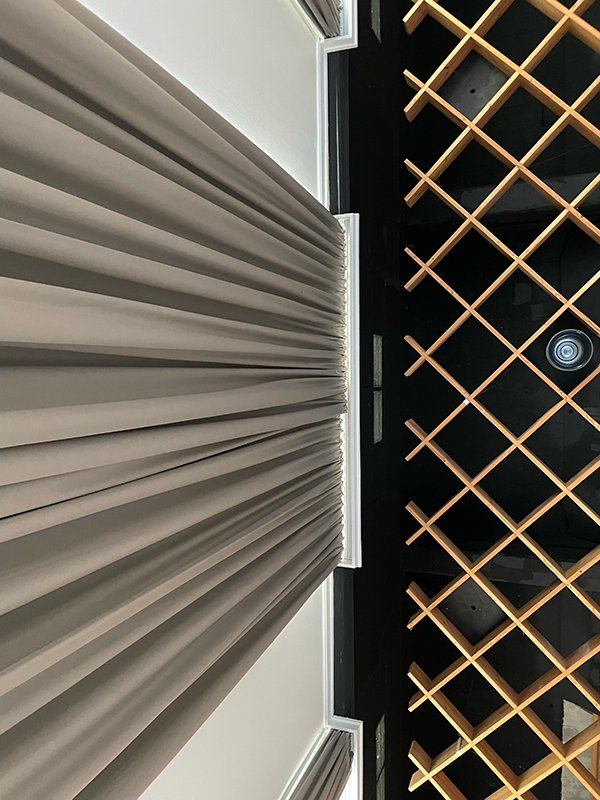 Beige pleated curtain hanging next to a black ceiling with a wooden lattice design.