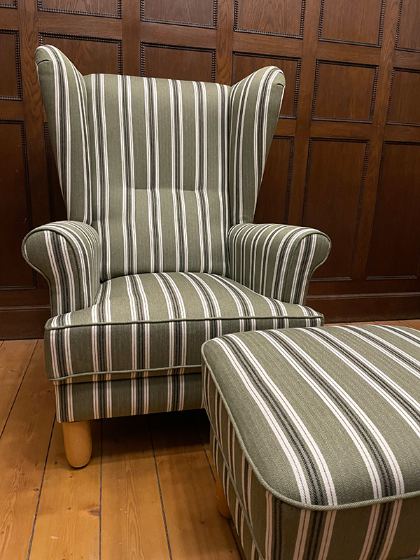 Green armchair with white and dark stripes next to a matching striped ottoman on a wooden floor with dark wood paneled walls.