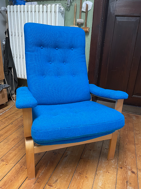 Blue cushioned armchair with wooden frame on a wooden floor in a room.